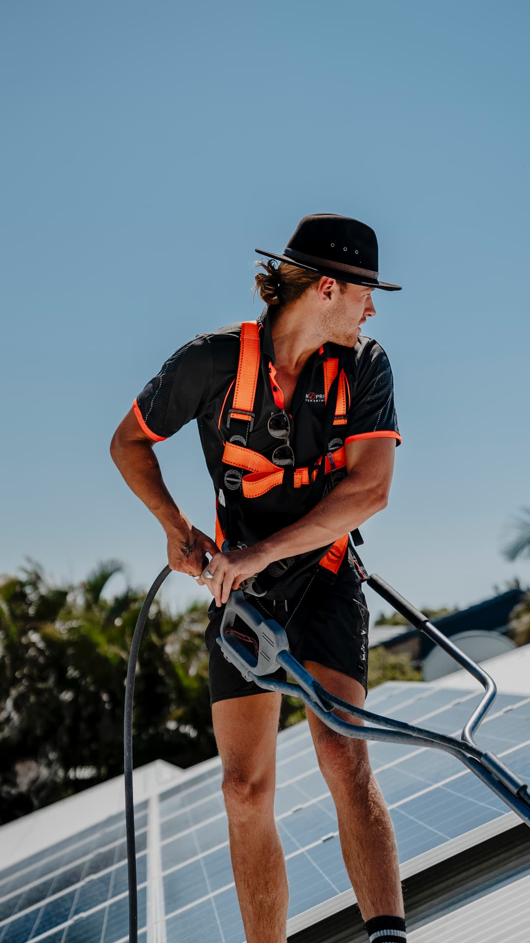 Owner operator in harness cleaning solar panels on a Sunshine Coast roof